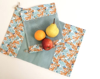 May include: A blue and white mesh produce bag with orange and blue floral print fabric trim. The bag is filled with a pear, an orange, and an apple.