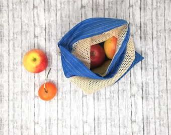 May include: A blue and beige reusable produce bag with apples and pears inside. The bag is sitting on a white wooden surface.