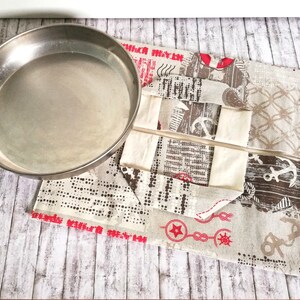 Puede incluir: Un molde para tartas de metal plateado sobre una tela beige con temática náutica. La tela tiene detalles en rojo, marrón y blanco. La tela tiene un patrón de anclas, cuerdas y nudos marineros.