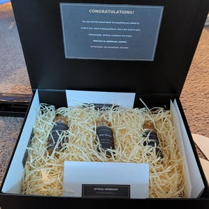 May include: A black gift box containing three small glass vials nestled in light-colored wood shavings. The lid interior features a printed card with the text: CONGRATULATIONS! You are now the proud owner of everything you asked for. A will to live. Some fucking patience. And a few fucks to give. Unfortunately, all three containers are empty. Welcome to adulthood, asshole. NO REFUNDS. NO EXCHANGES. NO HOPE.