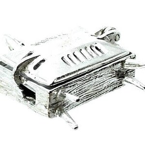May include: A small, silver-colored miniature barbecue grill with a hinged lid and four legs. The grill has a textured surface and decorative details, including a handle and vents on the lid. The overall design suggests a novelty or decorative item.