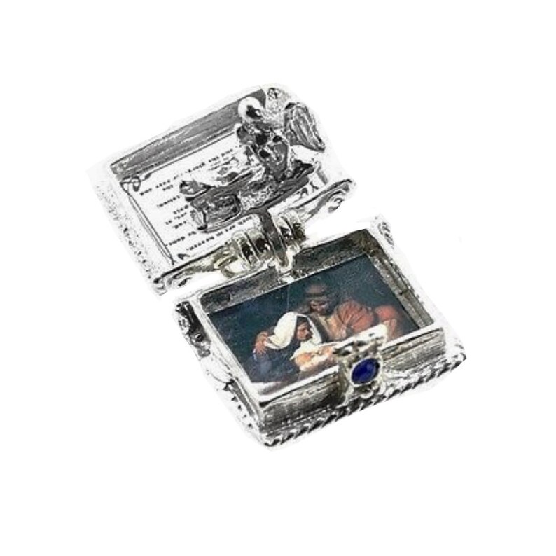 May include: A silver-toned, hinged pendant with an open rectangular compartment revealing a small image of a religious scene. The pendant has ornate detailing, including a small blue gem and a decorative top with text.
