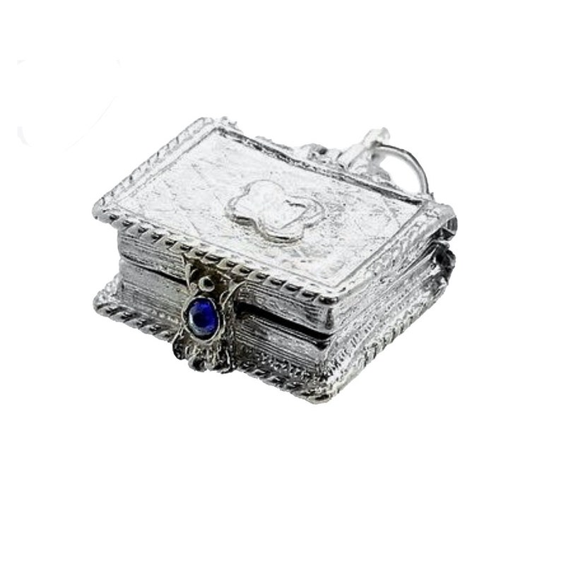 May include: A small, silver-colored book-shaped pendant with intricate embossed detailing. The pendant features a four-leaf clover design on the cover and a blue gemstone clasp. The edges are adorned with a decorative border, and a small loop is attached for a chain.