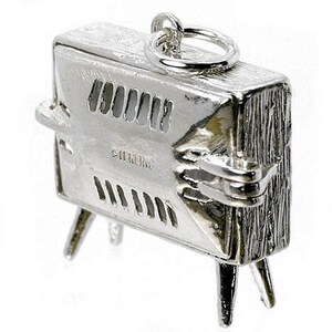 May include: A detailed, silver-toned charm in the shape of a vintage television set. The charm has a textured surface, vent-like openings, and small legs. The word "STERLING" is engraved on the front. A small ring is attached at the top.