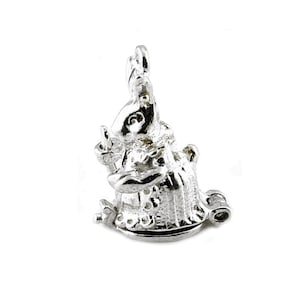 May include: A silver-colored charm in the shape of a rabbit wearing a dress and holding a small object. The charm has intricate details, including the rabbit's face, clothing, and the object it holds. The charm is designed to be attached to a bracelet or necklace.