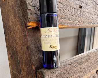Può includere: Un flacone roll-on in vetro blu cobalto con tappo nero ed etichetta color crema. L'etichetta riporta il testo Su Rein Anointing, BLEND 100% PURE, 10 ML / 1.0 OZ e una piccola illustrazione di un ramoscello d'ulivo in inchiostro dorato.