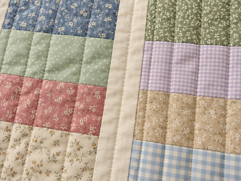 May include: A quilted fabric textile featuring a patchwork design of rectangular panels. The pattern includes blue, green, pink, and cream floral prints alongside lavender and blue gingham checks, all separated by a solid cream border.
