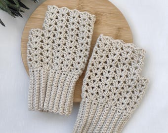 Op de afbeelding: Een paar beige vingerloze handschoenen met een gestructureerd haakpatroon, een geschulpte bovenrand en een geribbelde boord. De handschoenen zijn gemaakt met een herhalend schelpvormig steekpatroon over beide stukken.