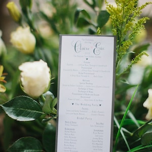 Könnte beinhalten: Ein graues Programm für eine Hochzeitszeremonie mit weißem Text. Das Programm listet die Reihenfolge der Ereignisse für die Hochzeitszeremonie von Claire und Eric auf. Das Programm listet auch die Namen der Hochzeitsgesellschaft auf.