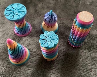 May include: A set of five multi-colored 3D printed objects featuring gradient hues of blue, pink, and yellow. The collection includes a spiral cone, a flower-topped cylinder, a pedestal with a floral base, a rounded topper, and a textured tube.
