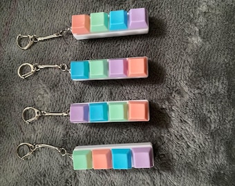 May include: Four rectangular keycap keychains, each featuring four square keys in pastel shades of peach, mint green, blue, and lavender. Each keychain has a white base and a silver-toned metal split ring attached by a short chain.