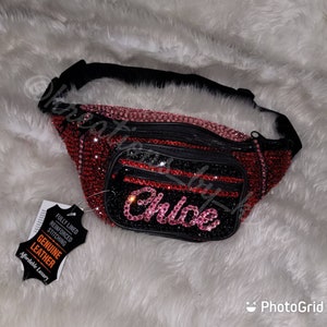 May include: A red and pink rhinestone fanny pack with the name "Chloe" in pink rhinestones. The fanny pack has a black strap and zipper, and a tag that says "Genuine Leather".