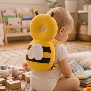 Puede incluir: Una mochila de protección para la cabeza con forma de abeja amarilla y negra, con alas blancas, dos antenas y correas ajustables. El cojín acolchado tiene un recorte circular en el centro y rayas horizontales.