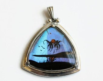 May include: A silver triangular pendant with a blue and purple butterfly wing inside. The butterfly wing has a black and orange design.