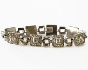 May include: A silver bracelet with a chain link design. Each link is adorned with clear rhinestones in a square shape.
