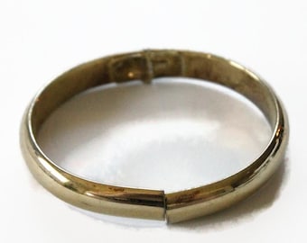 May include: A gold-toned bangle bracelet with a simple, rounded design. The bracelet is open and has a hinged clasp.