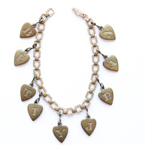 May include: A gold chain necklace with heart-shaped charms, each charm has a letter engraved on it. The letters spell out "BETTY."