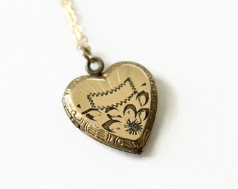 Pode incluir: Pingente dourado em forma de coração com uma corrente delicada. O medalhão apresenta desenhos florais e geométricos gravados. O pingente tem aproximadamente 2,5 cm de largura e pende de uma fina corrente dourada.
