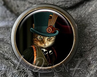 Könnte beinhalten: Schwarzer Badge-Rollenhalter mit Bronze-Lünette und einer runden, durchsichtigen Plastikabdeckung, die eine steampunk-artige Katze mit Zylinder und Schutzbrille zeigt.