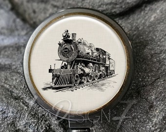 Könnte beinhalten: Schwarzer Badge-Rollenhalter mit Bronze-Lünette und einem weißen runden Einsatz mit einer Schwarzweiß-Illustration einer alten Dampflokomotive.