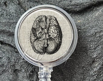 May include: A clear badge reel with a stainless steel bezel. The reel features a round, white, fabric-covered insert with a black and white anatomical illustration of a human brain.