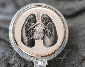 Könnte beinhalten: Transparente Badge-Rolle mit einer roségoldenen Lünette und einem runden, weißen Einsatz mit einer Schwarz-Weiß-anatomischen Illustration von Herz und Lunge.