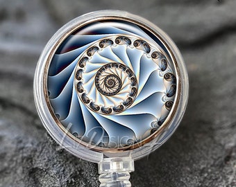 Könnte beinhalten: Transparente Badge-Rolle mit einer roségoldenen Lünette und einem blauen und weißen Spiralmuster. Die Rolle ist aus transparentem Kunststoff und hat einen Metallclip.