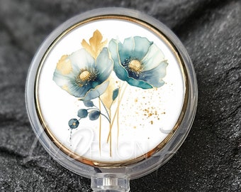 Puede incluir: Portatarjetas transparente con bisel dorado, con un diseño floral en verde azulado y dorado. El portatarjetas tiene un cuerpo de plástico transparente y un cordón retráctil. El texto "Liz Design 7" está en la parte superior y "Clear Badge Reel With Gold Bezel" en la inferior.