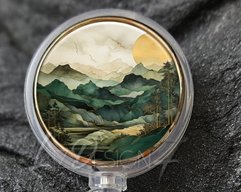 Könnte beinhalten: Transparente Badge-Rolle mit goldener Einfassung und einem runden, farbenfrohen Bild einer Berglandschaft mit einer untergehenden Sonne hinter den Bergen.