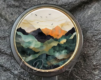 Puede incluir: Carrete de insignia negro con bisel dorado. El carrete presenta un diseño redondo con una pintura de paisaje de montañas en tonos verdes, naranjas y negros. El texto "Liz Design 7" está en la parte superior.