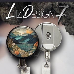 May include: A silver retractable badge reel with a round, black, printed design featuring a landscape scene with mountains, water, and a sunset. The design is surrounded by a silver metal frame. The reel has a white fabric strap.