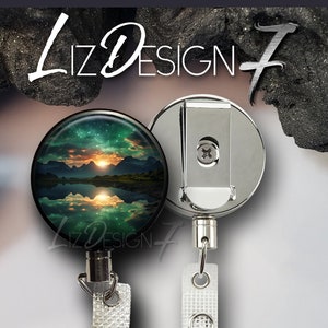 May include: A retractable badge reel with a scenic landscape design. The round reel features a sunset over mountains reflected in a lake, with the text "Liz Design 7". The reel has a silver metal clip and a clear plastic strap.