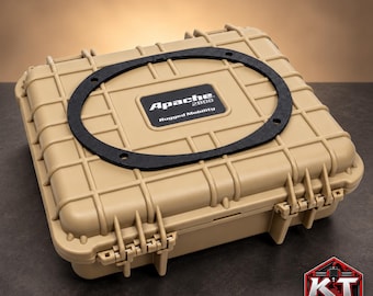 Può includere: Una custodia protettiva rigida rettangolare color beige con un motivo esterno a griglia. Il coperchio presenta un anello di guarnizione nero di forma ovale e un'etichetta centrale con la scritta Apache 2800 Rugged Mobility. È visibile un logo KT Customz rosso e nero.
