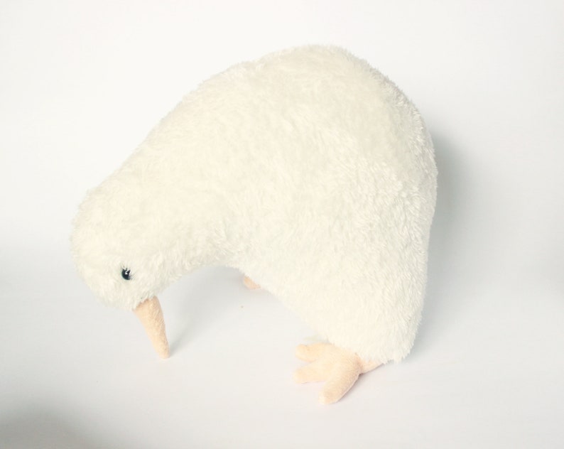 May include: A plush, cream-colored kiwi bird toy. The soft toy has a long, curved beak, small black eyes, and tiny feet. The kiwi is a flightless bird native to New Zealand. The toy is designed to resemble the bird.