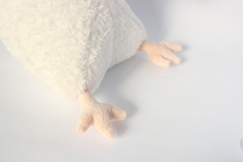 May include: A plush white chicken toy with soft, fluffy feathers. The chicken has light pink feet with three toes. The toy is designed to be soft and cuddly, perfect for children or as a decorative item.