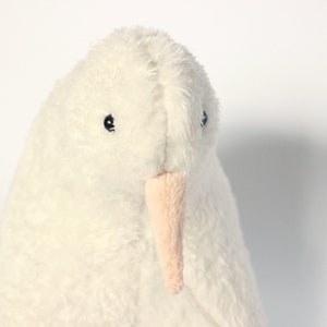 May include: A plush, white bird with a soft, textured appearance. The stuffed animal has small black eyes and a light pink beak. The bird's body is a creamy white color, and it appears to be made of a fluffy material.
