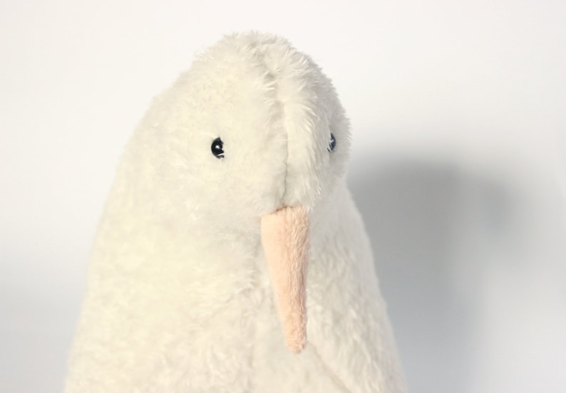 May include: A plush, white bird with a soft, textured appearance. The stuffed animal has small black eyes and a light pink beak. The bird's body is a creamy white color, and it appears to be made of a fluffy material.
