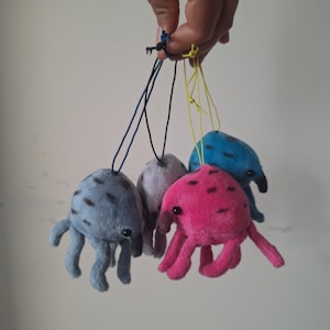 May include: A set of four small plush octopus toys in blue, pink, grey, and light blue, each featuring black spots, a rounded head, multiple dangling tentacles, and a thin string loop attached to the top for hanging as a decorative ornament.