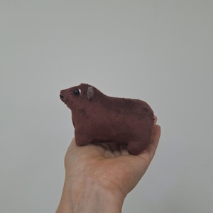 Puede incluir: Un pequeño juguete de peluche marrón con forma de oso. El juguete tiene una pequeña nariz negra y ojos negros.