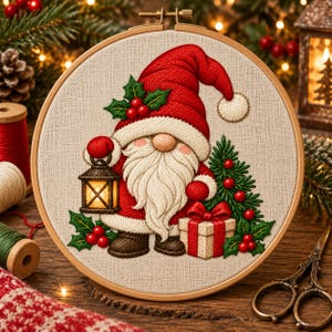 Puede incluir: Un bastidor de bordado circular con un panel de tela que muestra un diseño bordado de un gnomo con gorro y abrigo rojos, sosteniendo un farol encendido y un regalo. El gnomo tiene barba blanca, acebo y un árbol de Navidad.
