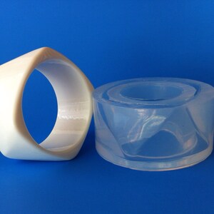 May include: Two white and clear plastic molds for making jewelry. The white mold is a ring shape and the clear mold is a round shape.