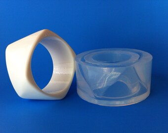 May include: Two white and clear plastic molds for making jewelry. The white mold is a ring shape and the clear mold is a round shape.