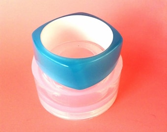 May include: A square-shaped, blue and white bangle bracelet. The bangle is made of plastic and has a smooth, glossy finish.