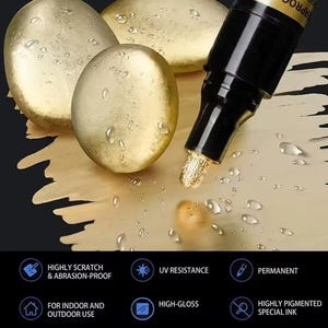 May include: Close-up of a gold metallic marker with a black cap, dispensing gold ink onto a surface. The image shows three gold-colored, pebble-shaped objects. Text on the image indicates the marker is highly scratch and abrasion-proof, UV resistant, permanent, and high-gloss.