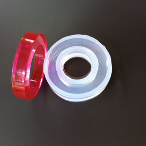 May include: Two silicone molds for crafting. One is clear and the other is a vibrant red. Both molds are ring-shaped with a smaller inner circle.