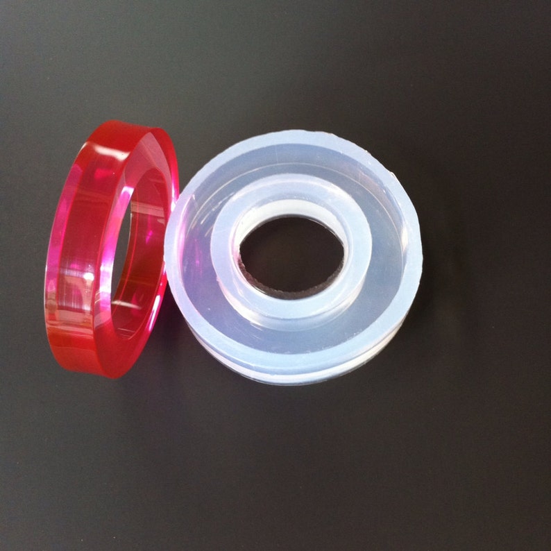May include: Two silicone molds for crafting. One is clear and the other is a vibrant red. Both molds are ring-shaped with a smaller inner circle.