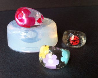 May include: Three resin rings with different designs. One ring has a red and white floral design, another has a ladybug design, and the third has a floral design with yellow, blue, and purple flowers.
