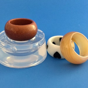 May include: Three resin rings, one brown, one white with black polka dots, and one beige. The rings are on a clear silicone mold.