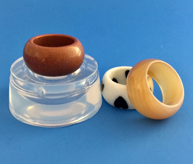 May include: Three resin rings, one brown, one white with black polka dots, and one beige. The rings are on a clear silicone mold.
