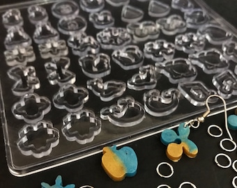 May include: A clear plastic mold with various shapes for making earrings. The mold is filled with blue and gold resin earrings, including a star, a flower, and an apple. There are also jump rings and earring hooks.